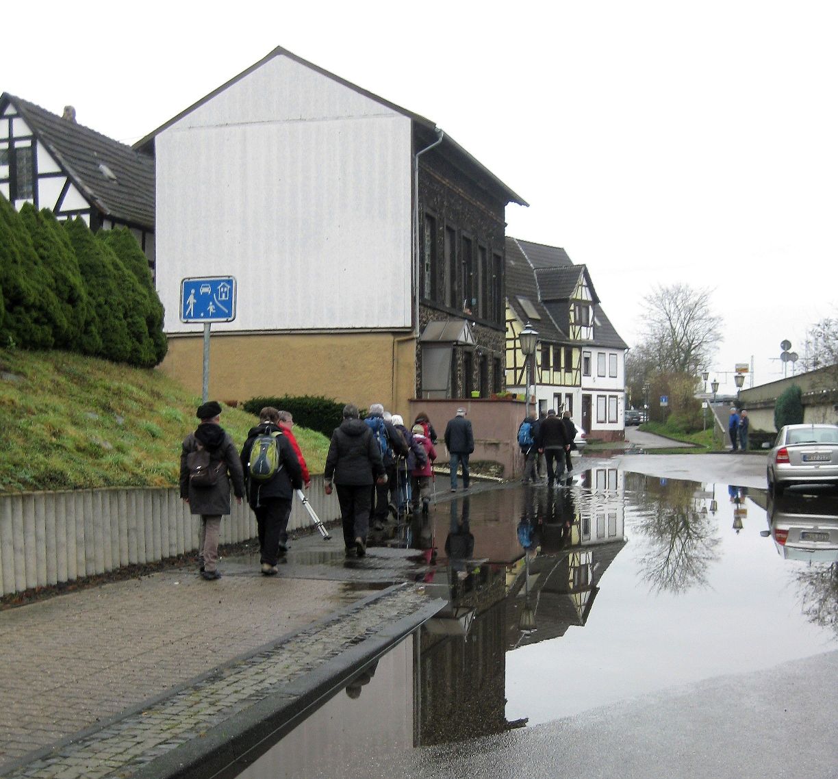 Eine riesige Wasserpfütze steht auf Straße und Bürgersteig. Die Pilger müssen ganz am Rand einzeln dieses Hindernis meistern. (c) Elisabeth Bußmann Eine riesige Wasserpfütze steht auf Straße und Bürgersteig. Die Pilger müssen ganz am Rand einzeln dieses Hindernis meistern.