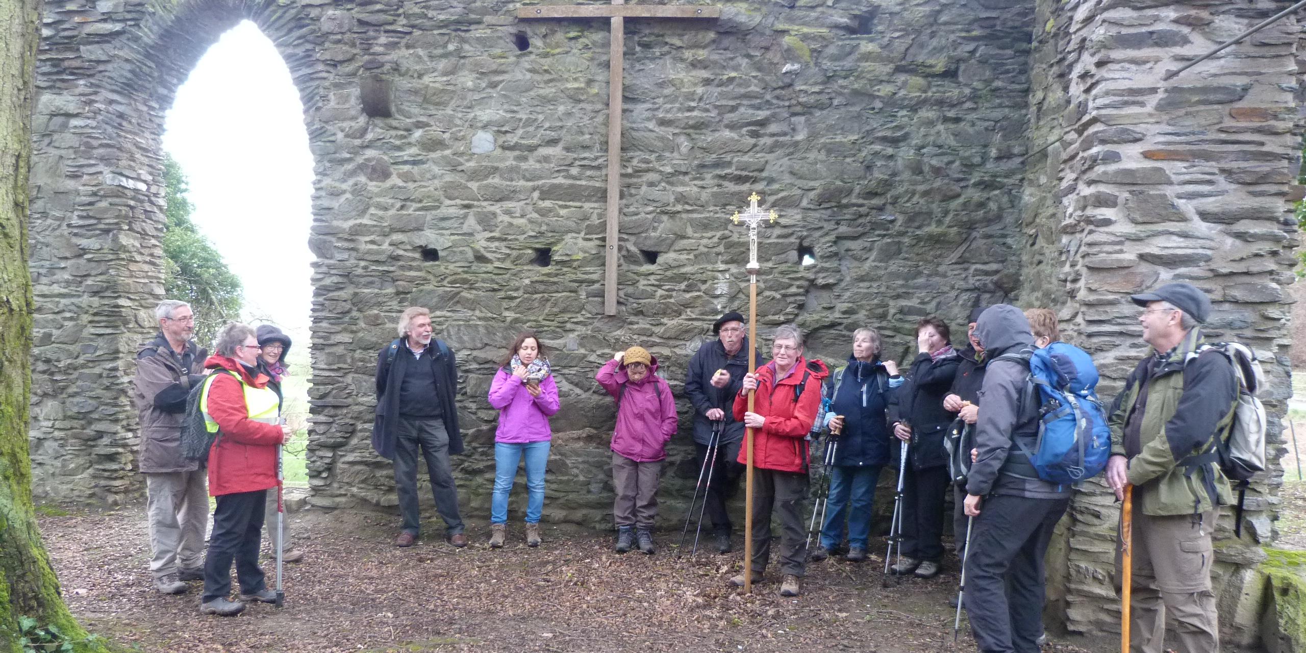Die Teilnehmen stehen versammelt zum Impuls in der Ruine. An einer erhaltenen Steinwand ist ein großes schlichtes Wandkreuz angebracht.