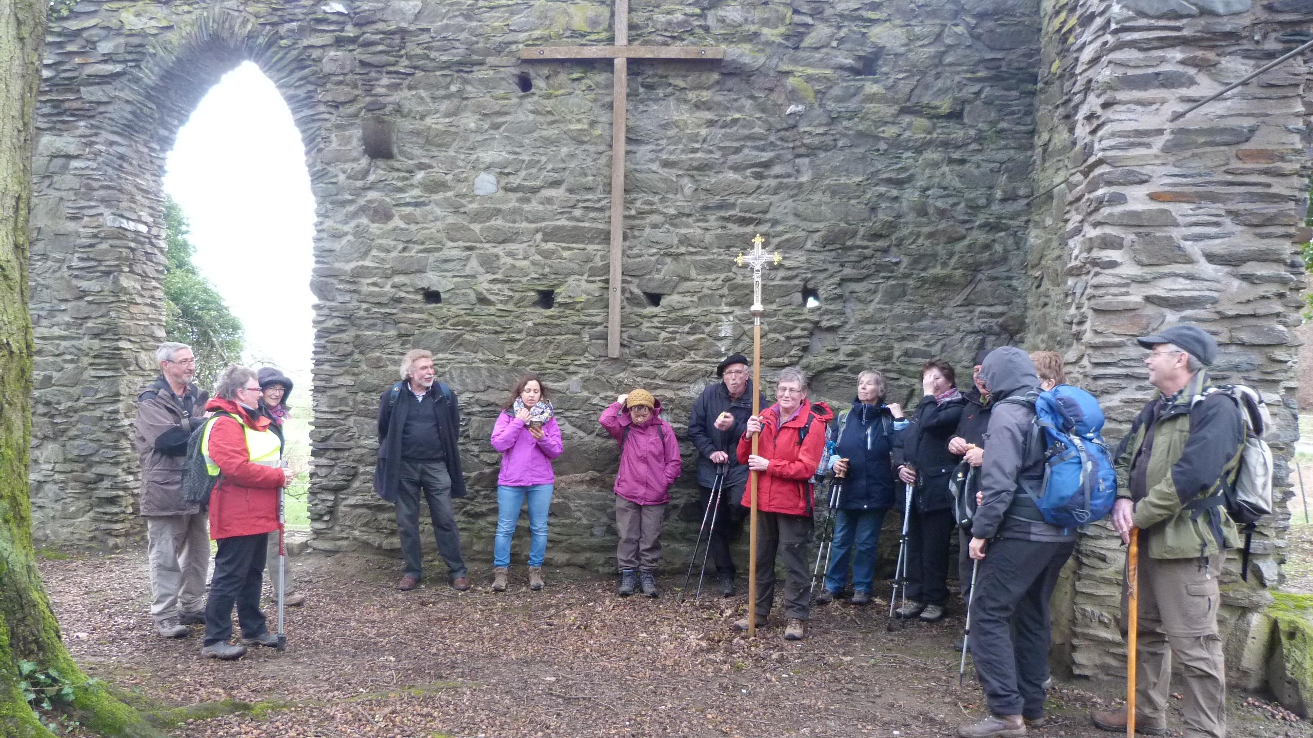 Die Teilnehmen stehen versammelt zum Impuls in der Ruine. An einer erhaltenen Steinwand ist ein großes schlichtes Wandkreuz angebracht.