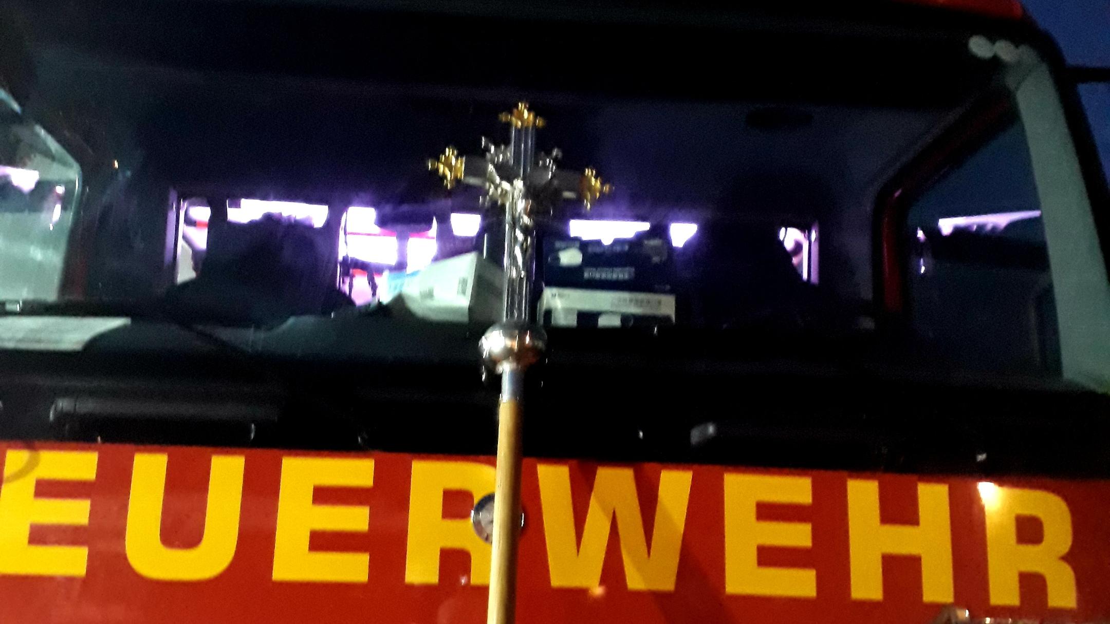 Feuerwehrauto von vorne, daran angelehnt das Vortragekreuz des Martinsweges