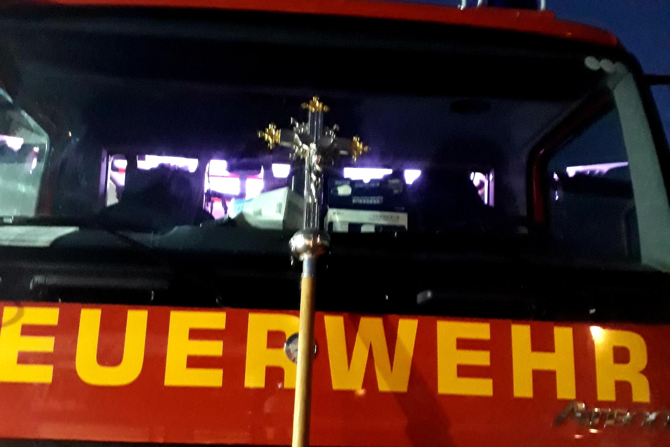 Feuerwehrauto von vorne, daran angelehnt das Vortragekreuz des Martinsweges