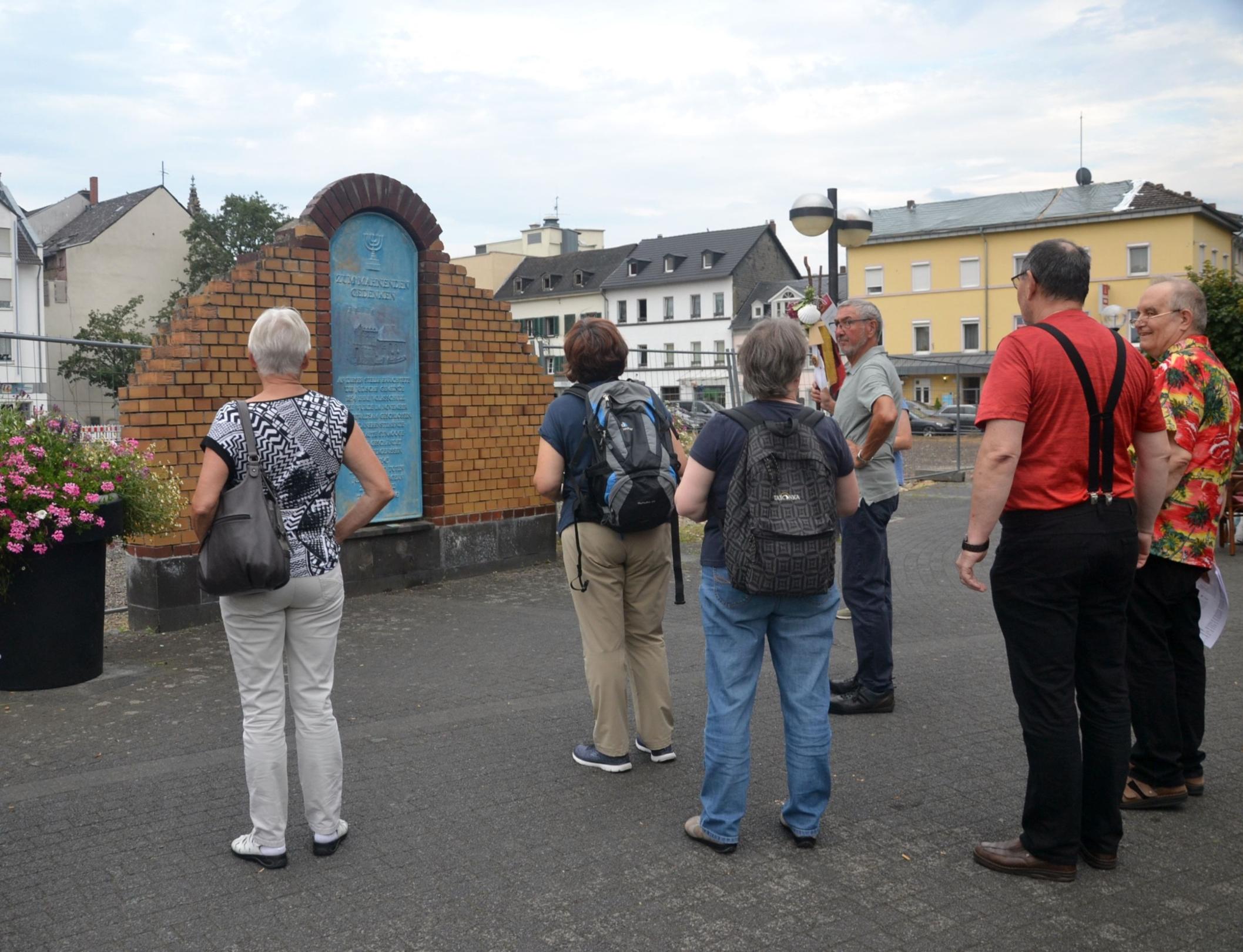 Die Gedenkstätte an der ehemaligen jüdischen Synagoge in Neuwied besteht auf eine hellblauen Platte mit Text und Menora, eingefasst von gelben Mauersteinen.