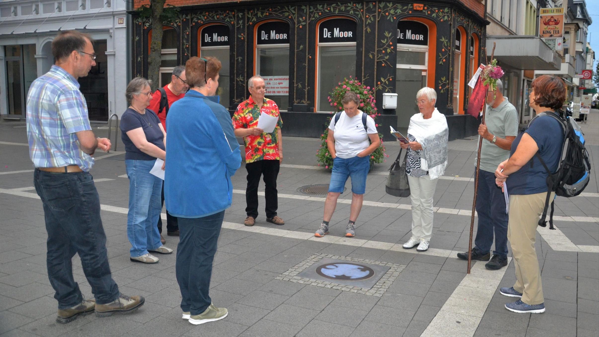 Die Pilgergruppe steht um den 'Engel der Kulturen', der im Straßenpflaster eingelassen ist.