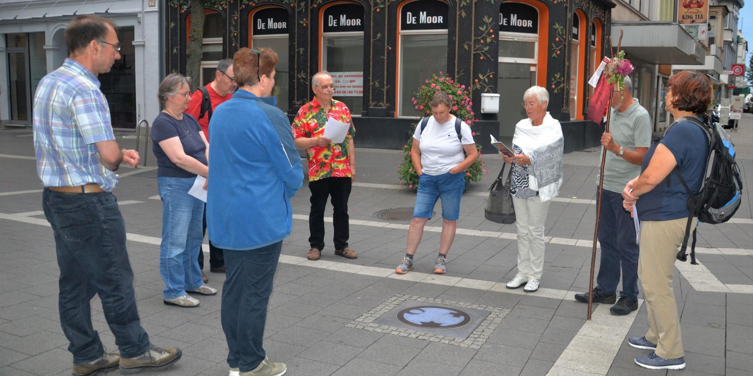 Die Pilgergruppe steht um den 'Engel der Kulturen', der im Straßenpflaster eingelassen ist.