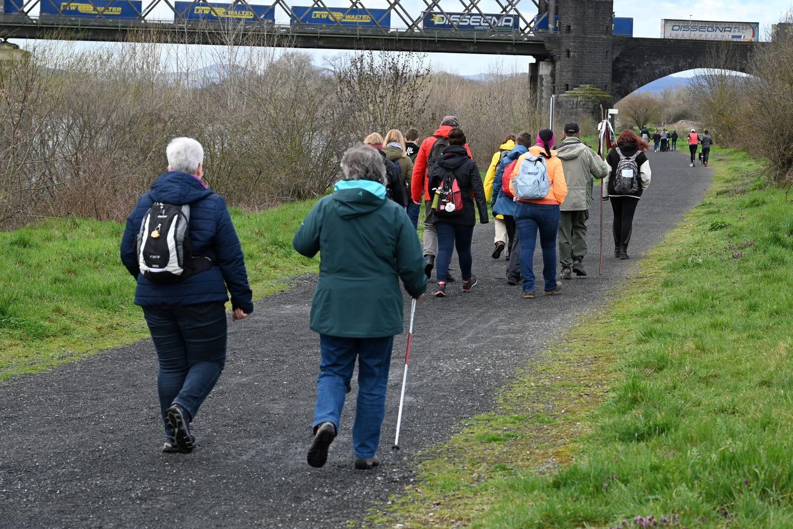 Die Pilgergruppe wandert auf einem Pfad, der unter der Urmitzer Eisenbahnbrücke (auf Engerser Seite) hindurchführt.