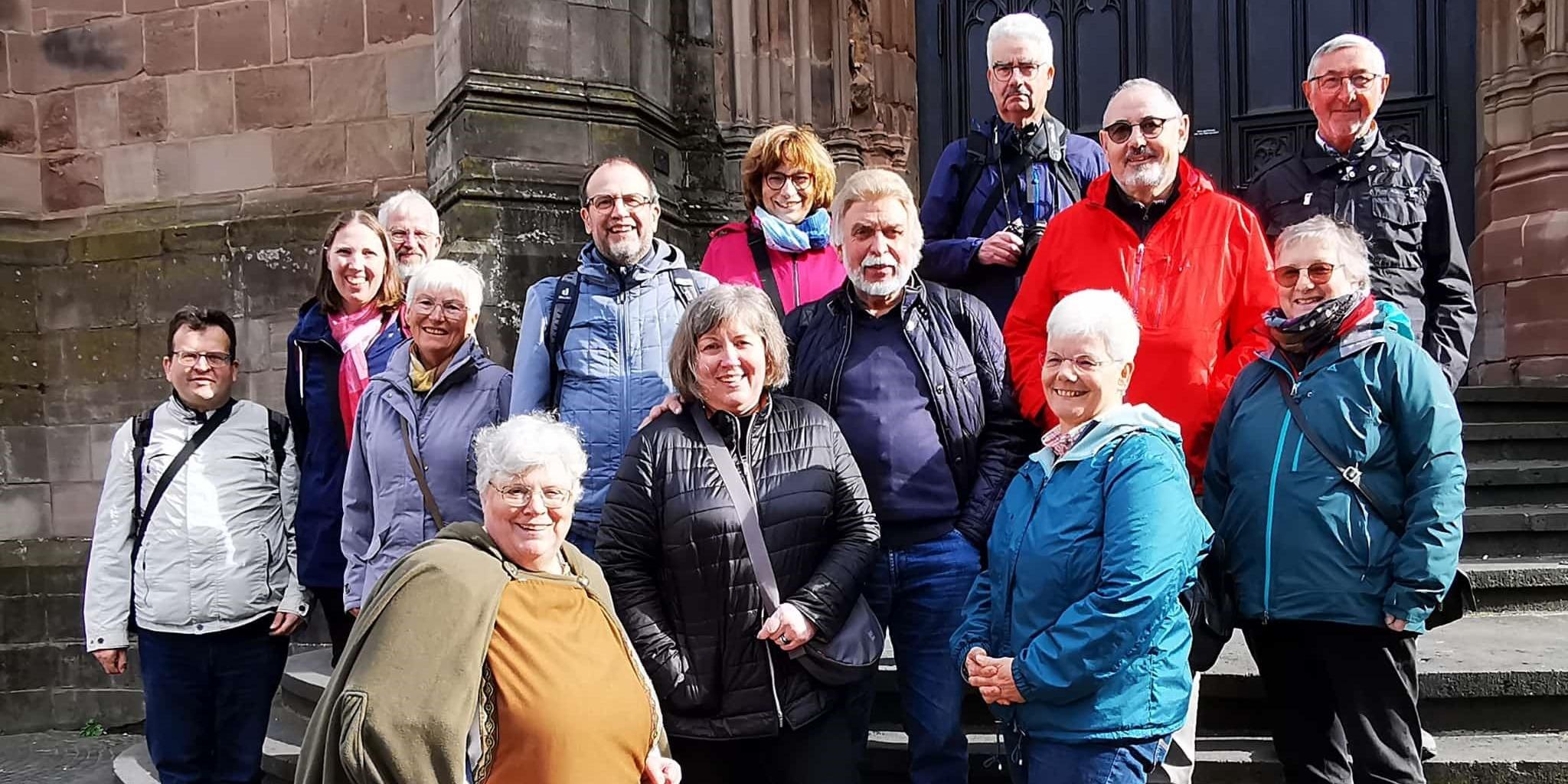 Dreizehn Menschen im fortgesetzten Alter stehen zusammen mit einer Pilgerführerin auf den Stufen zur Basilika.