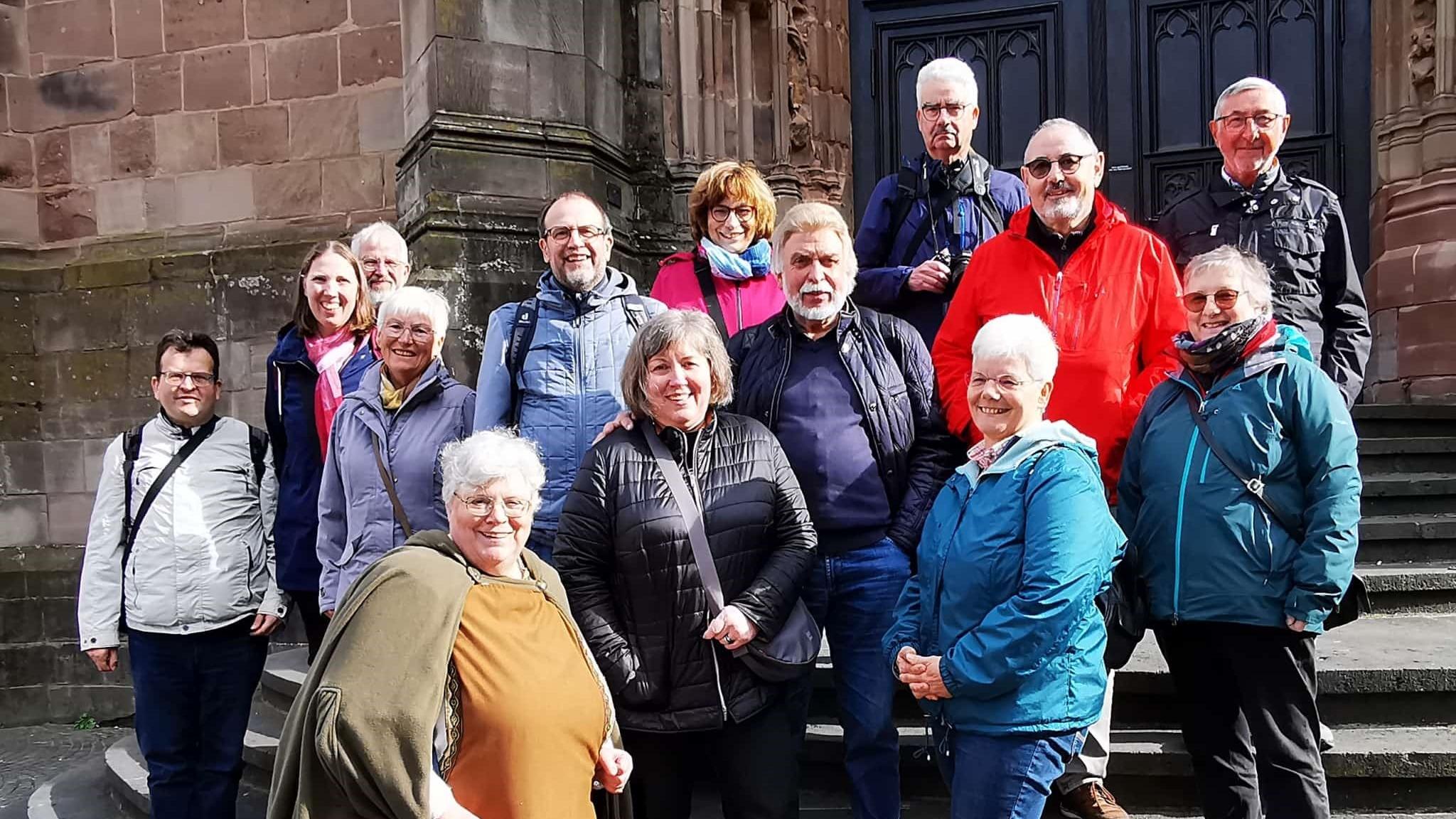 Dreizehn Menschen im fortgesetzten Alter stehen zusammen mit einer Pilgerführerin auf den Stufen zur Basilika.