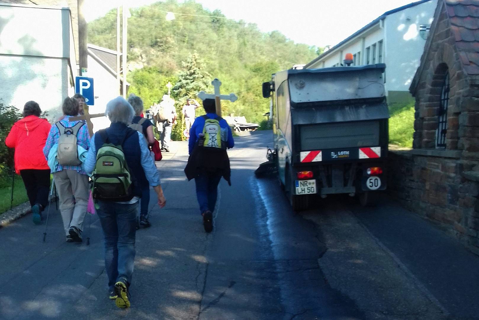 Die Pilgergruppe mit mehreren Tragekreuzen passiert in Ariendorf einen Straßenreinigungswagen.